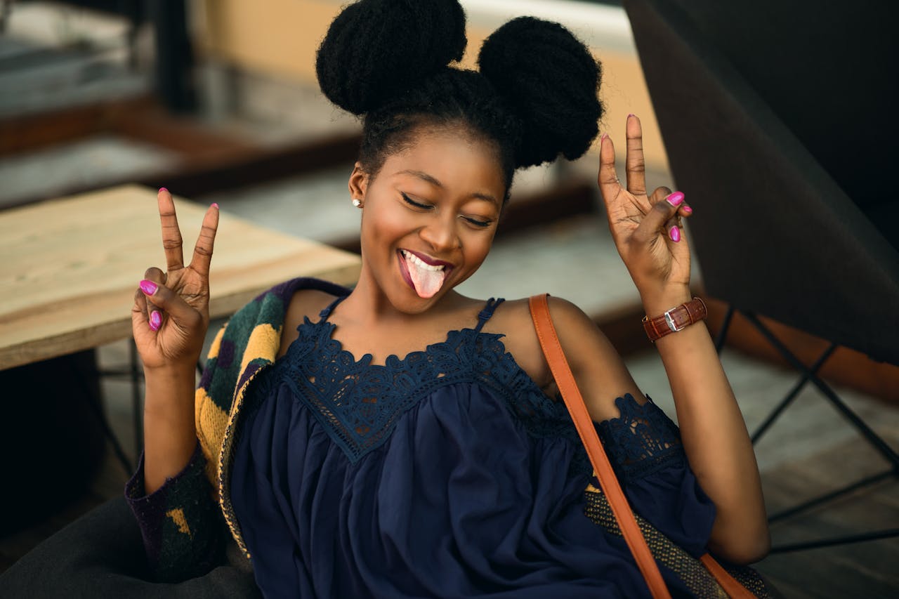 Joyful young woman making peace signs and posing playfully indoors.